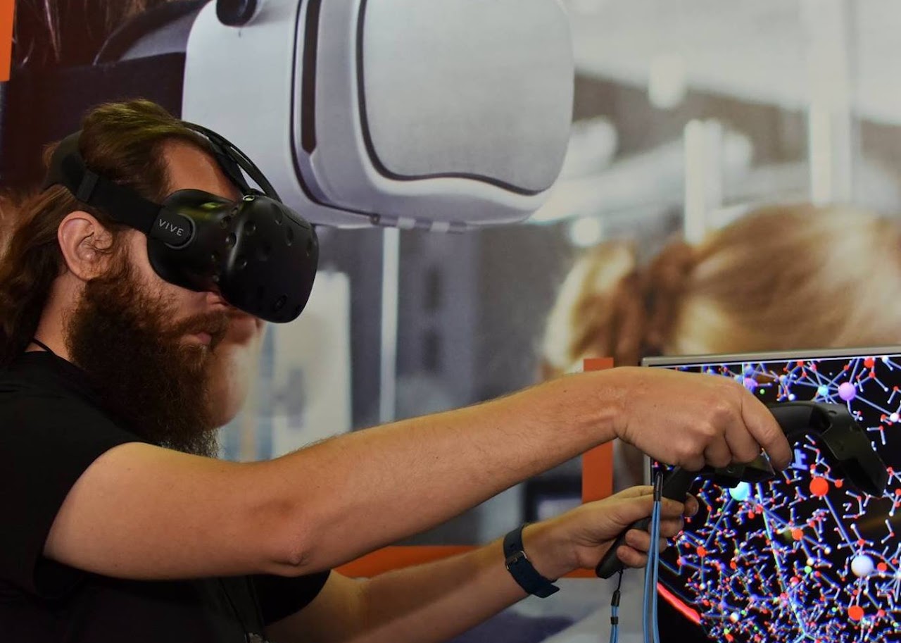 James M. de Almeida usando óculos de realidade virtual diante de uma visualização molecular